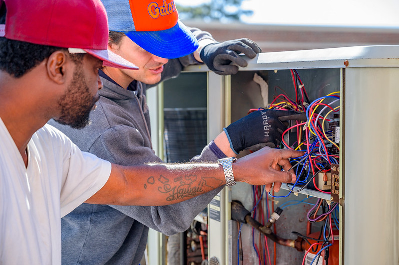 Two men point at portions of an air conditioning condenser