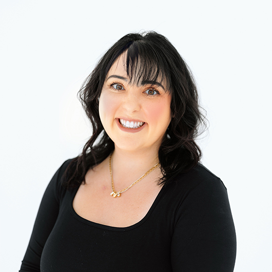 Woman with black hair wearing a gold necklace and black shirt