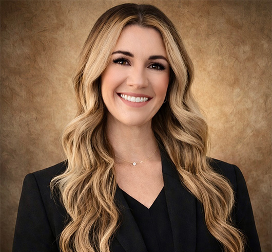 Smiling woman with wavy blond hair wearing a dark suit