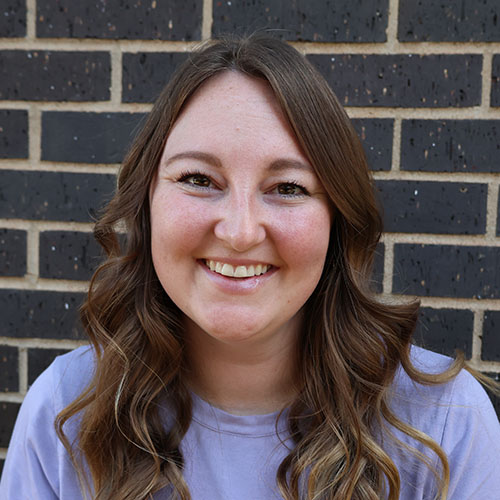 Woman with wavy medium brown hair in front of a brick wall