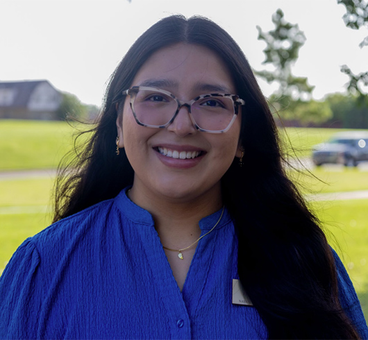 Woman with long black hair wearing a blue shirt and speckled glasses