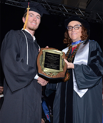 Two people in robes hold a wooden plaque