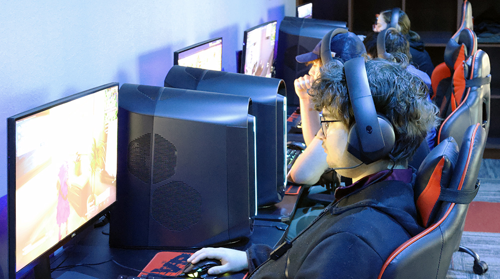 Four students sit at gaming computers, playing a video game