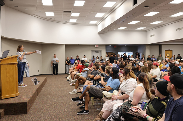 Speaker stands on stage, talking to a full crowd of students