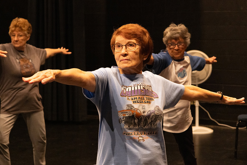 Three women stretch out their arms during a fitness class