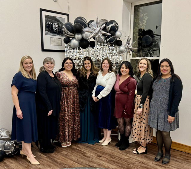Photo of women standing in front of a silver and black display with balloons