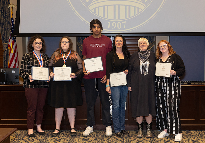 Redlands students and an instructor are standing holding the certificates they received for their academic achievements.
