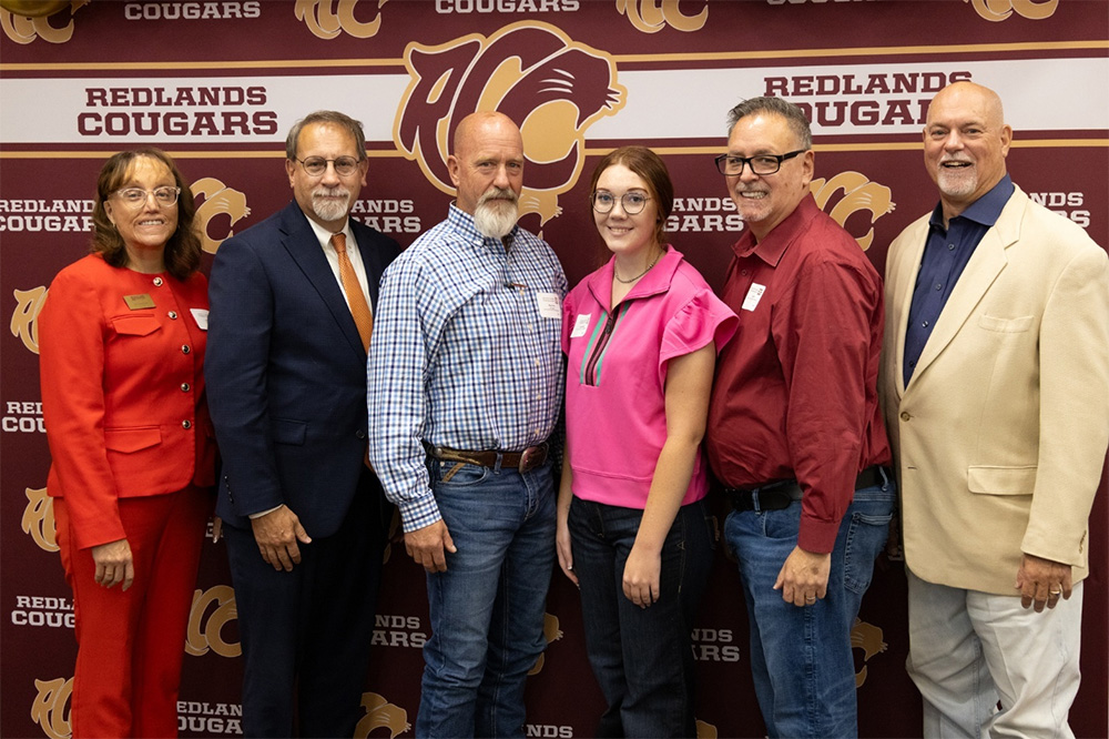 Six people stand in front of the Redlands photo backdrop