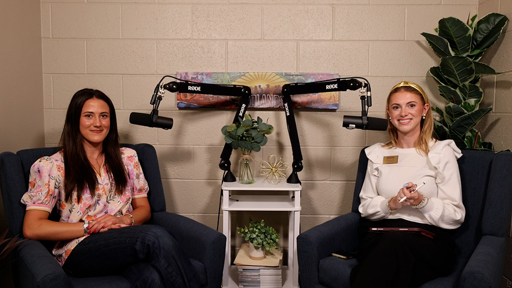 Two women smile and sit next to microphones