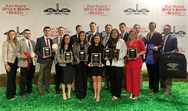 A group of students, standing on grass, smile with their awards