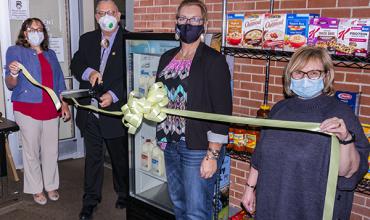 President Bryant cuts the ribbon unveiling the new cooler donated to the student food pantry.